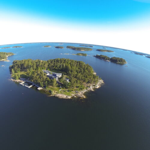 Flygbild över en skärgårdsö med bebyggelse och bryggor.